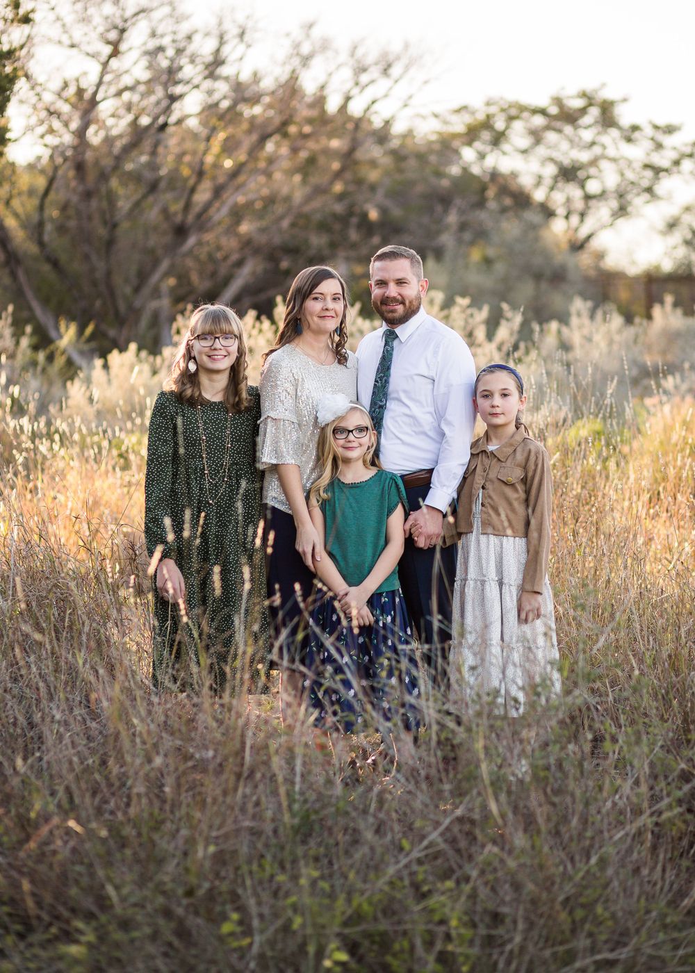Family of five posed together in tall golden grass during sunset.