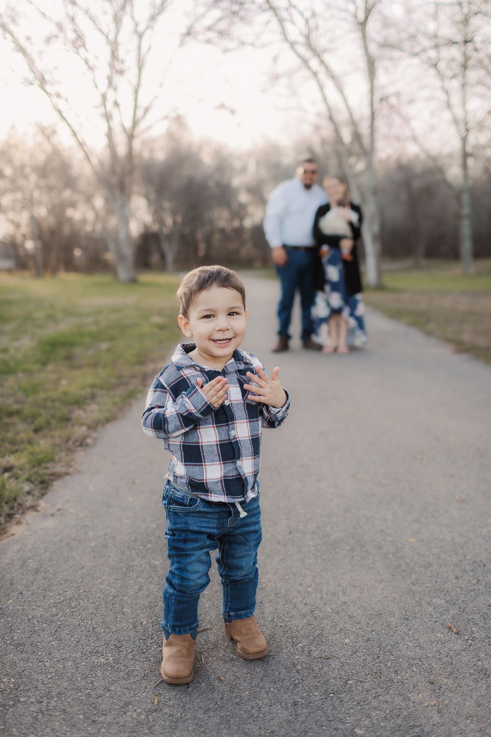 Small child walking on a paved path in the park wearing plaid and jeans.