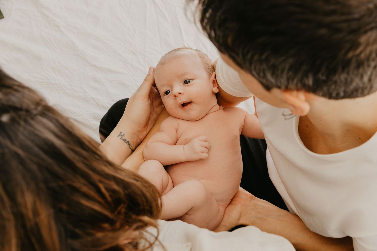 Tender moment of parents caring for their newborn baby lying on white bedding.