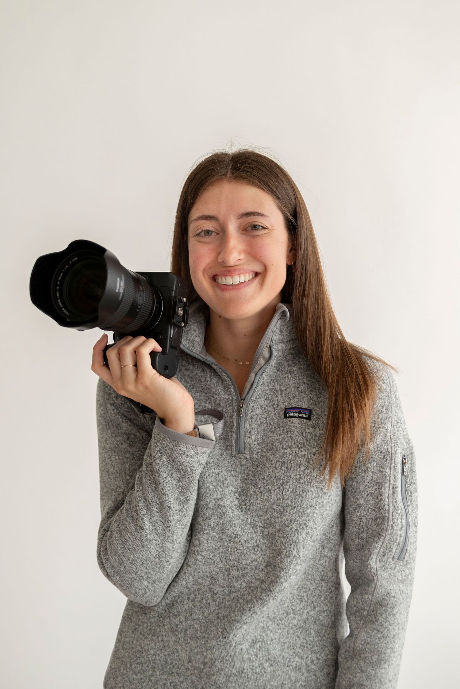 A Metro Detroit photographer holding a professional camera with telephoto lens against white background and laughing for a studio photoshoot