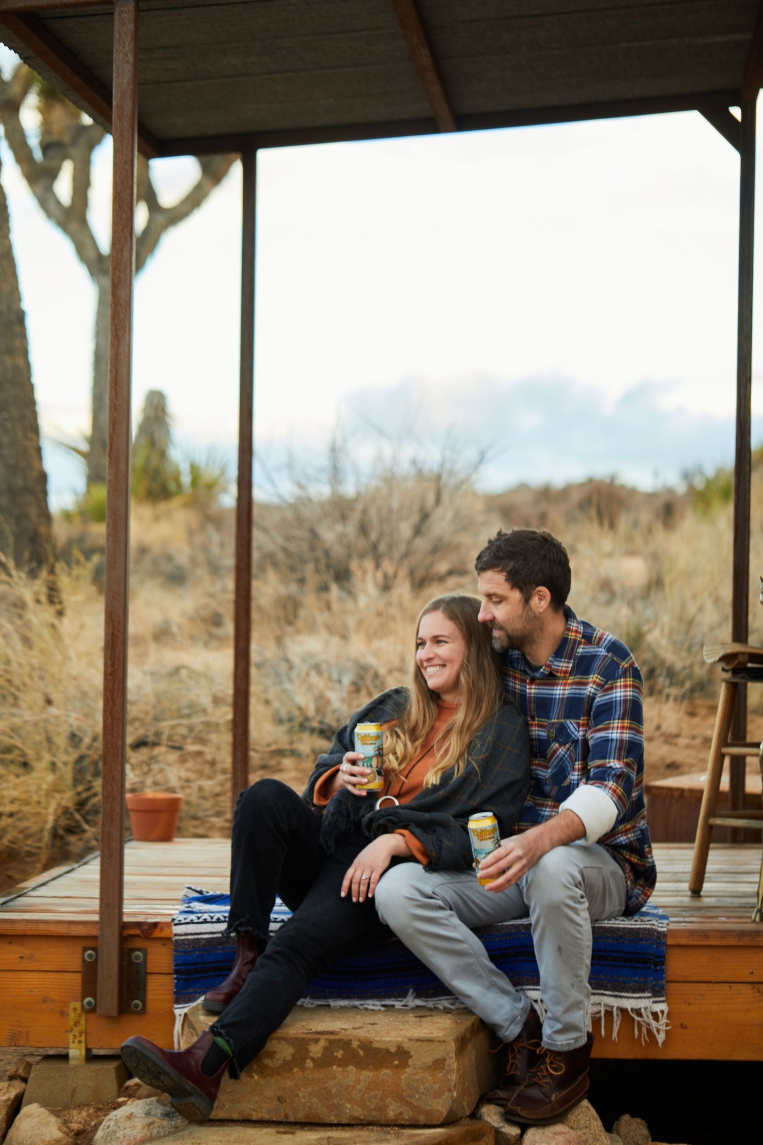 A casual couple sharing drinks on a rustic porch overlooking desert mountains.