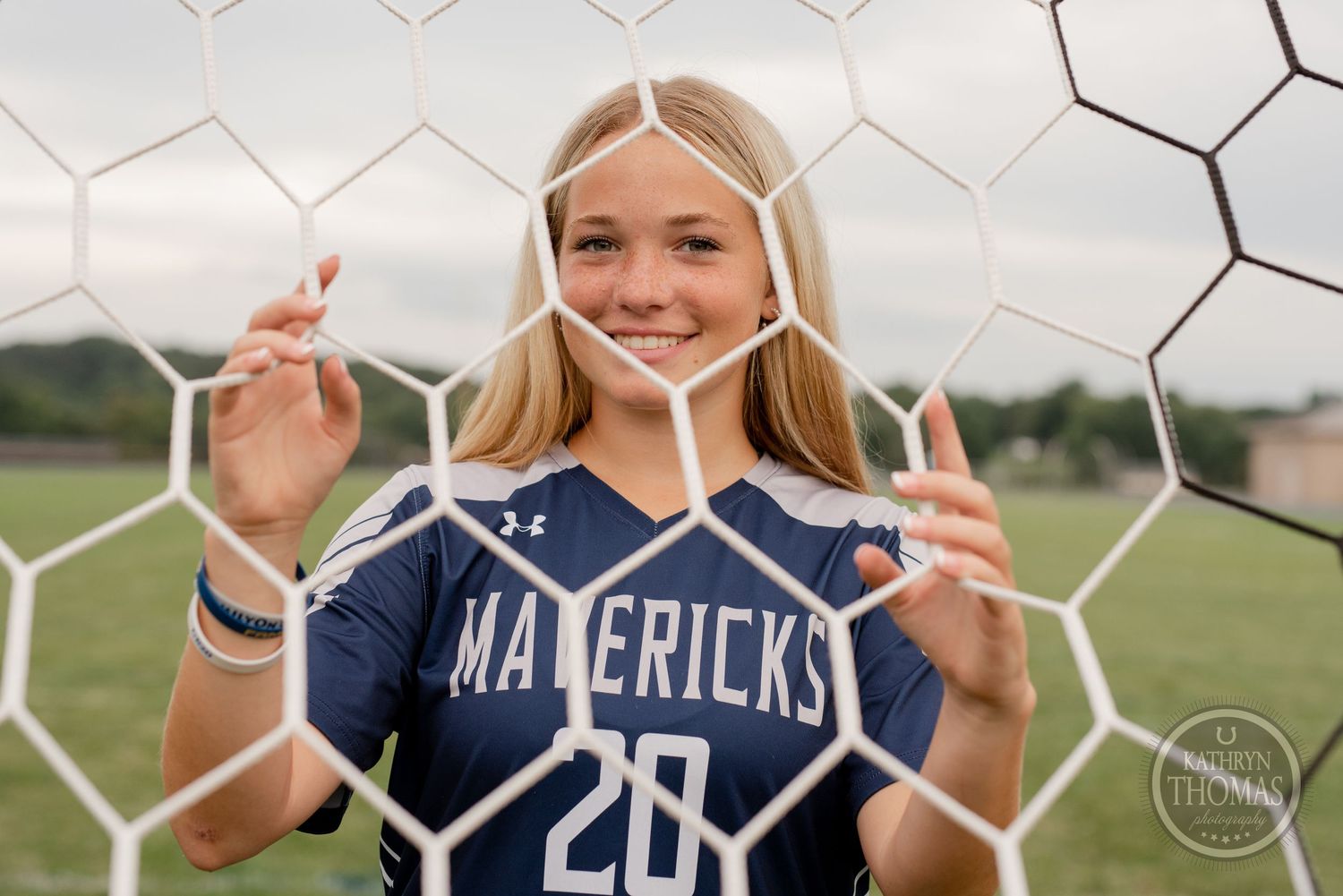 Soccer player in navy jersey poses playfully through goal net mesh on field.