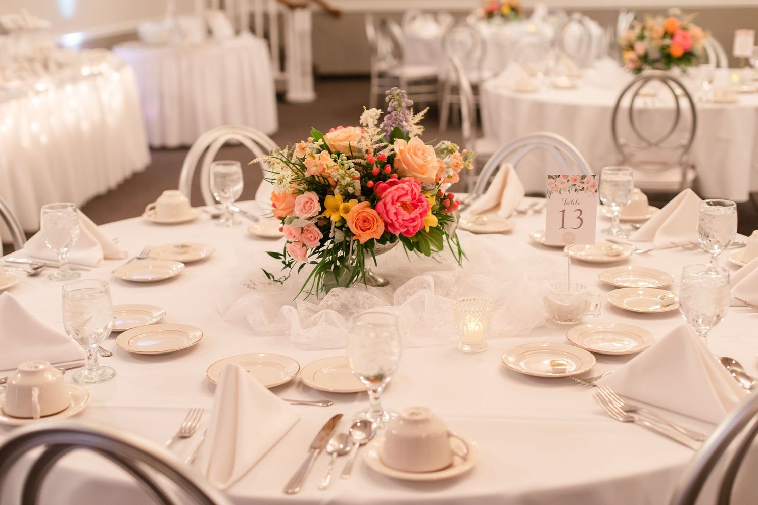 White and coral floral centerpieces adorn round tables set with fine china and glassware.
