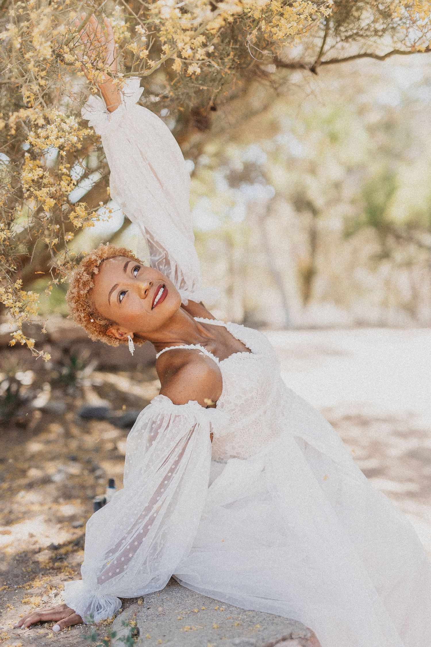 Person in flowing white dress twirling under blooming spring tree branches.