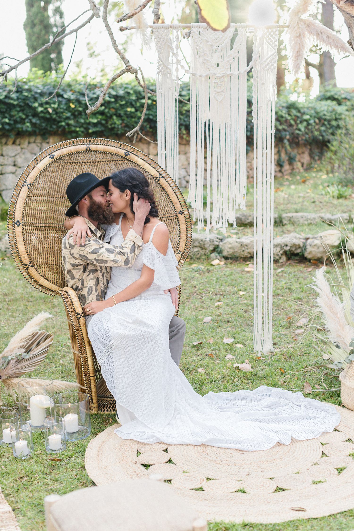 A bride and groom kiss whilst sitting on a wicker peacock chair