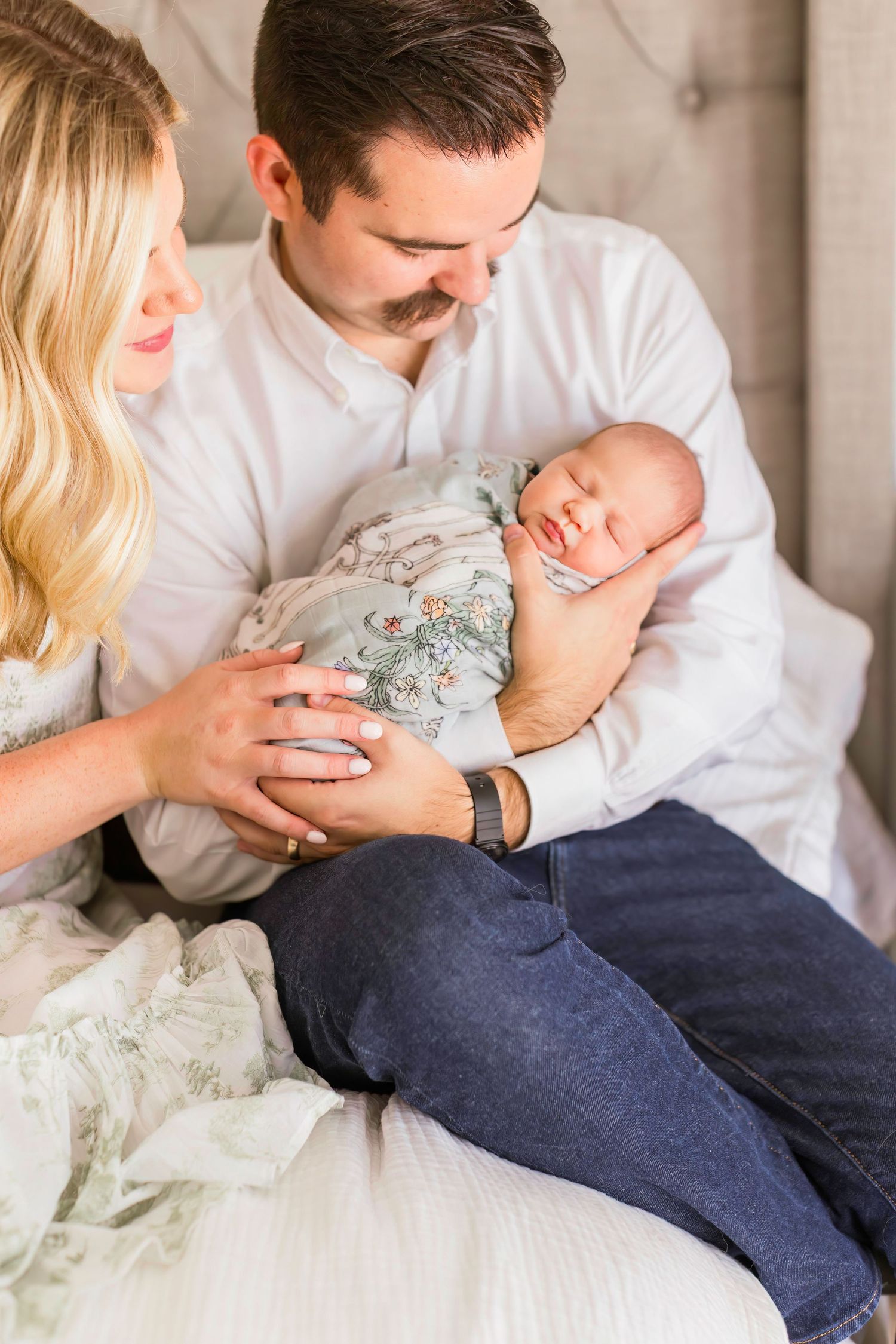 Parents gazing lovingly at their sleeping newborn wrapped in floral pattern.