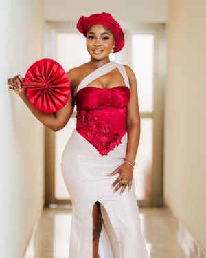 Woman in a red and white formal gown posing in a hallway with a matching red accessory.