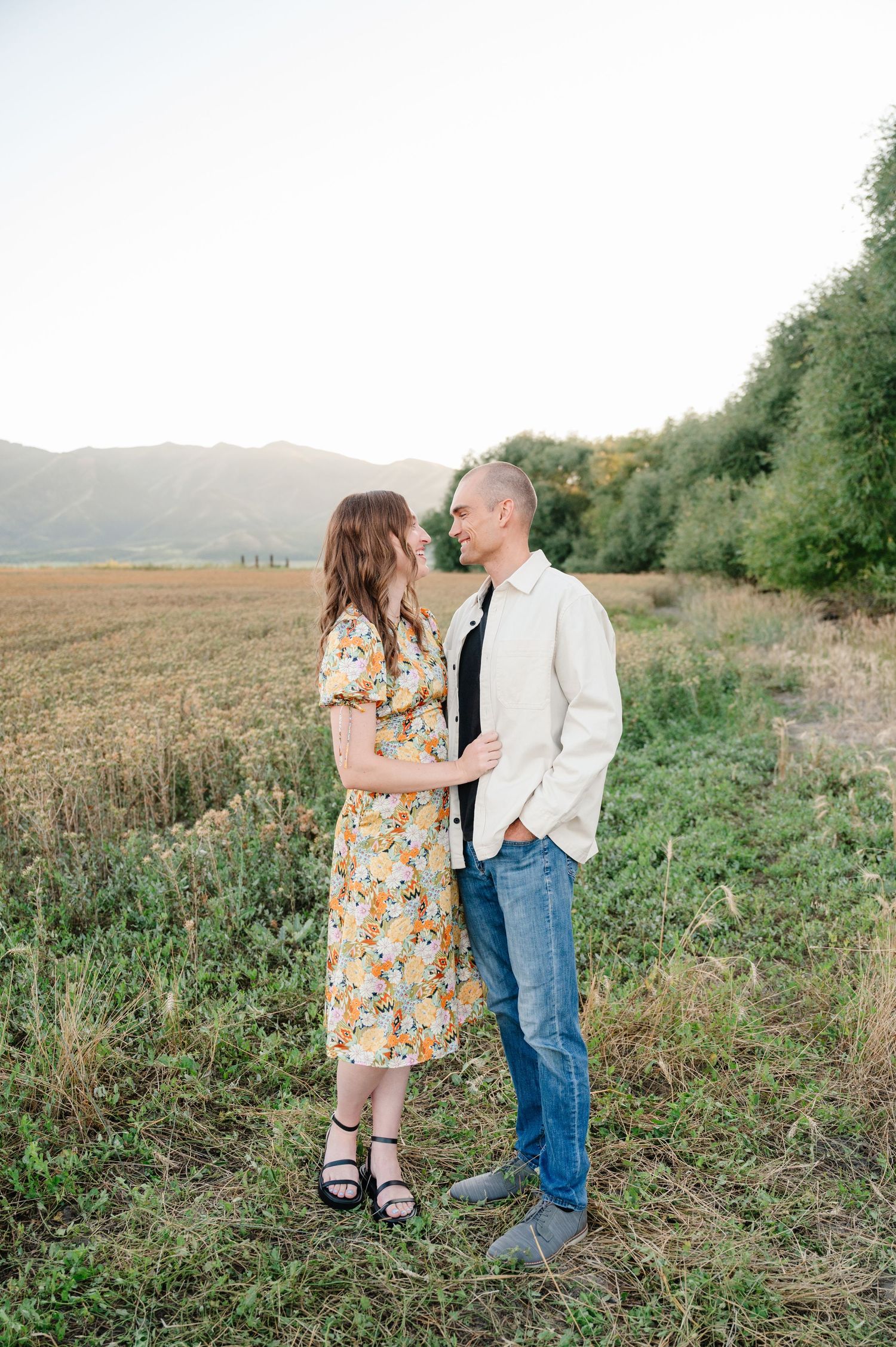 Couple sharing an intimate moment in a rustic field with mountains on the horizon.