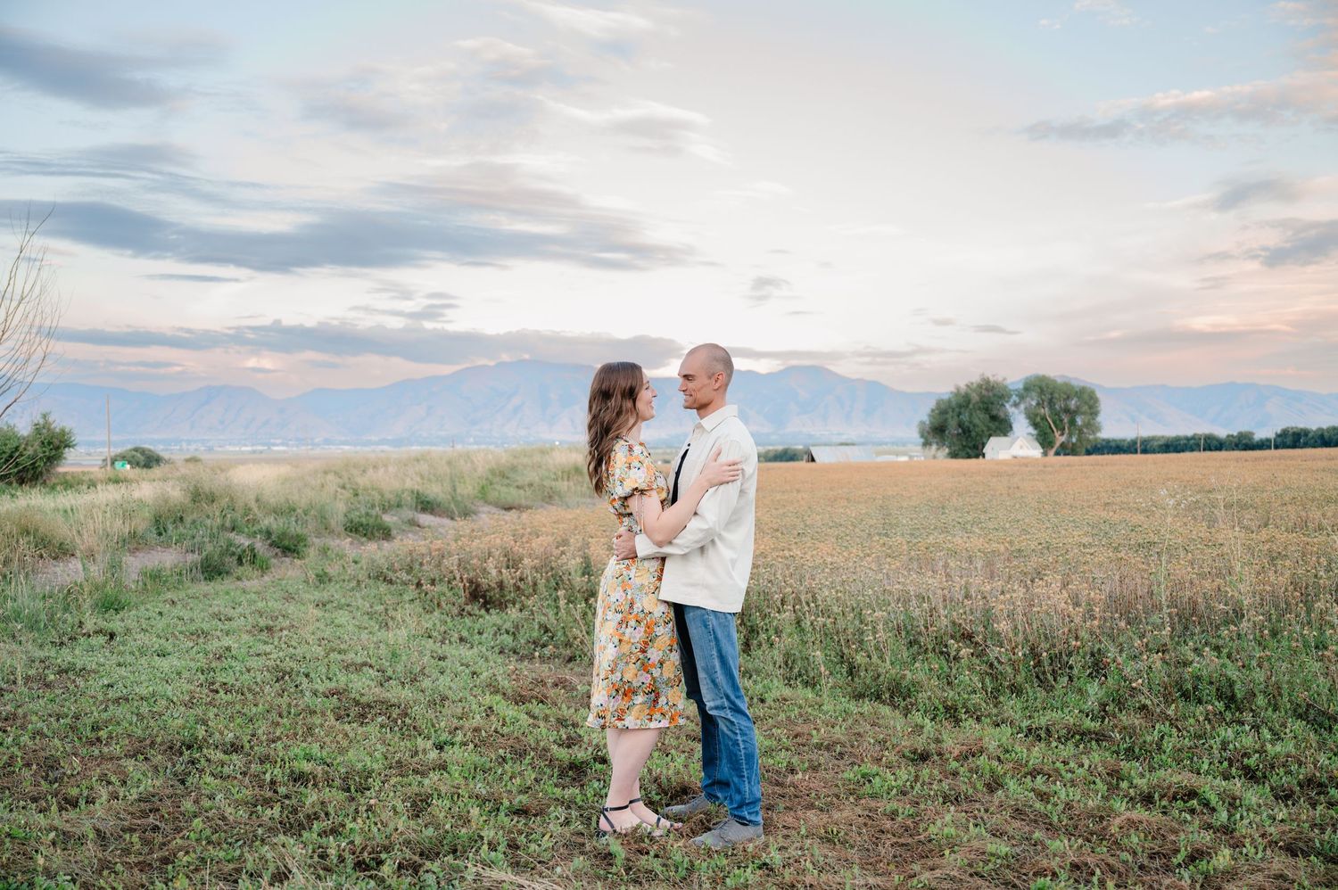 Couple enjoying a tender moment in a meadow during sunset with mountain backdrop.