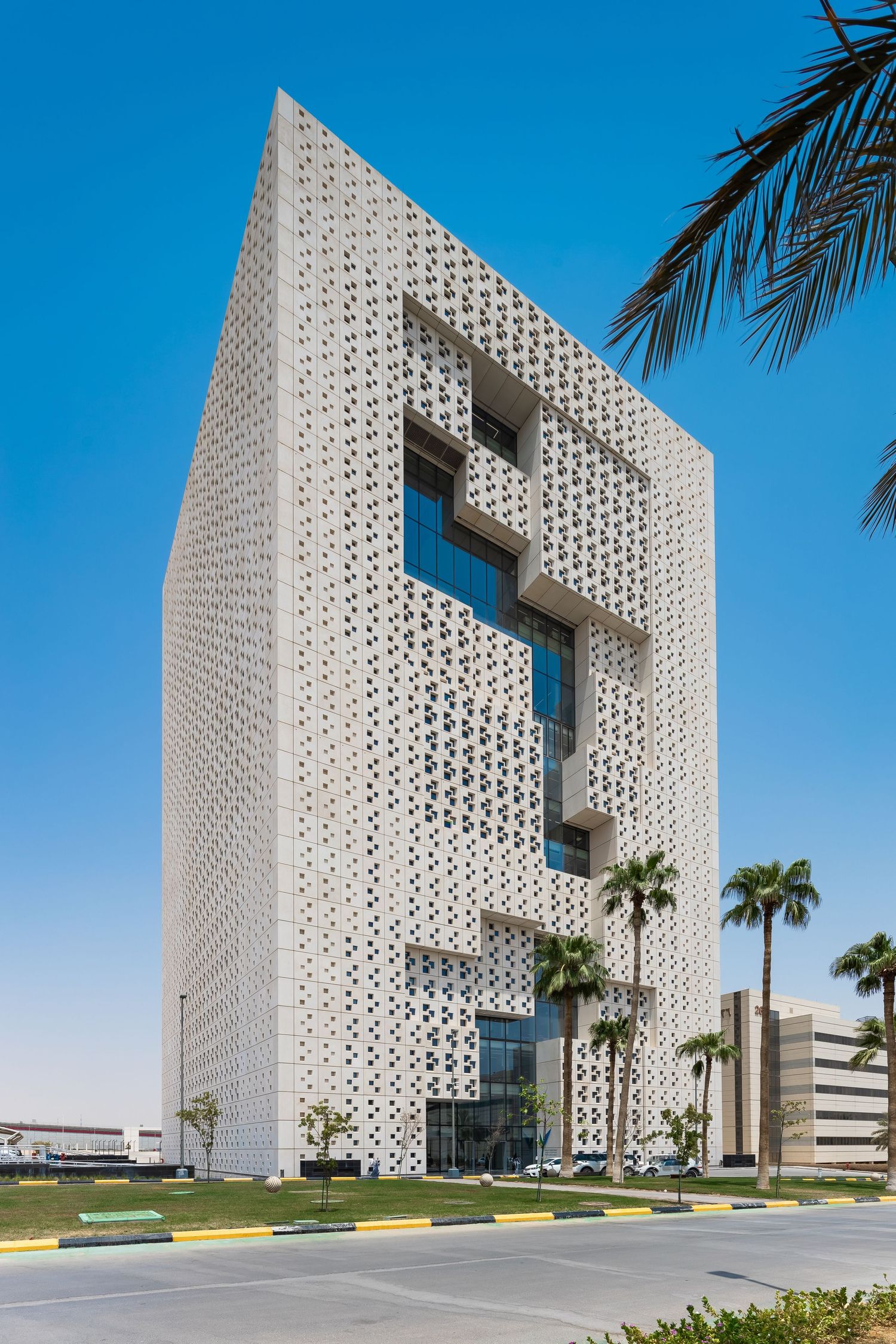 Modern office building with distinctive perforated white facade and palm trees.