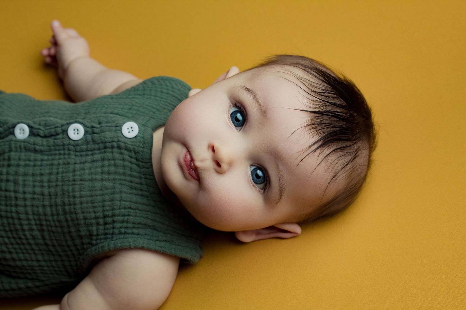 Baby in green sweater poses against golden yellow background in a series of candid expressions.