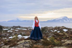 Traditional Nordic dress against snowy mountain landscape at sunset.