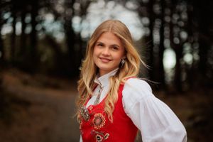 Traditional Nordic folk costume with red embroidered vest and white blouse in a forest setting.