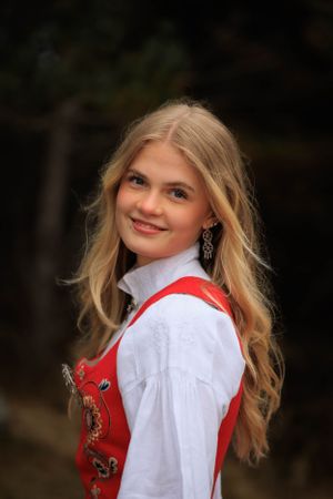 Portrait in traditional Norwegian bunad with ornate red vest and white blouse.