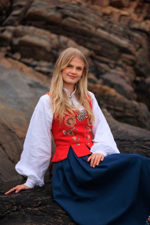 Traditional Norwegian dress portrait on rocky coastal terrain.