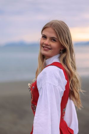 Traditional Norwegian bunad costume photographed against scenic coastal backdrop at sunset.