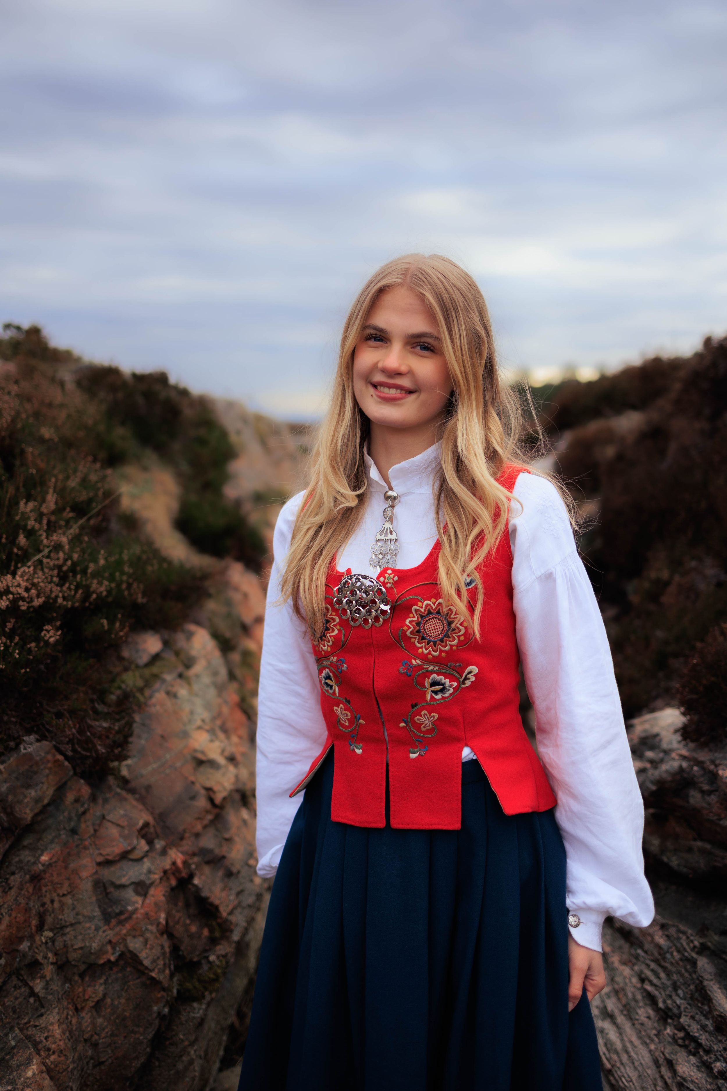 Traditional Nordic folk dress with decorative red vest posed on rocky terrain.