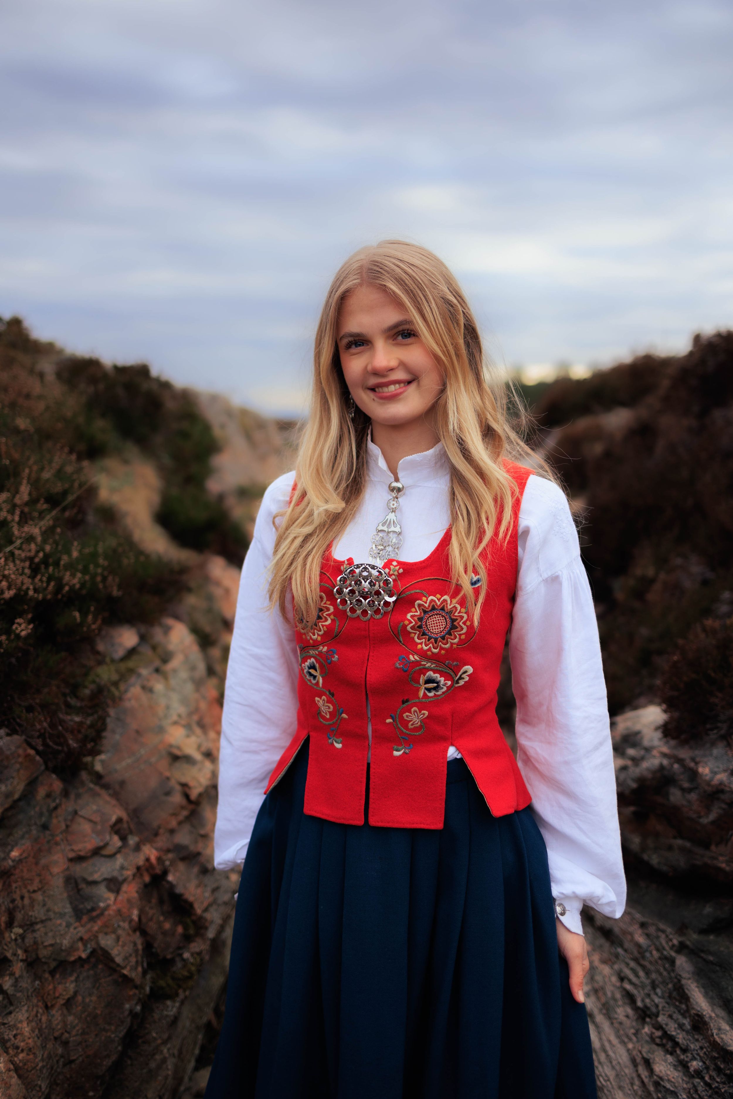 Nordic traditional costume with red embroidered bodice and navy skirt on rocky landscape.