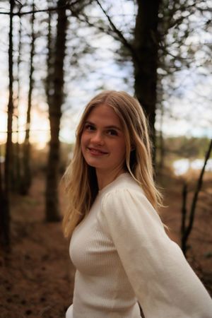Sunset portrait in white sweater among pine trees.