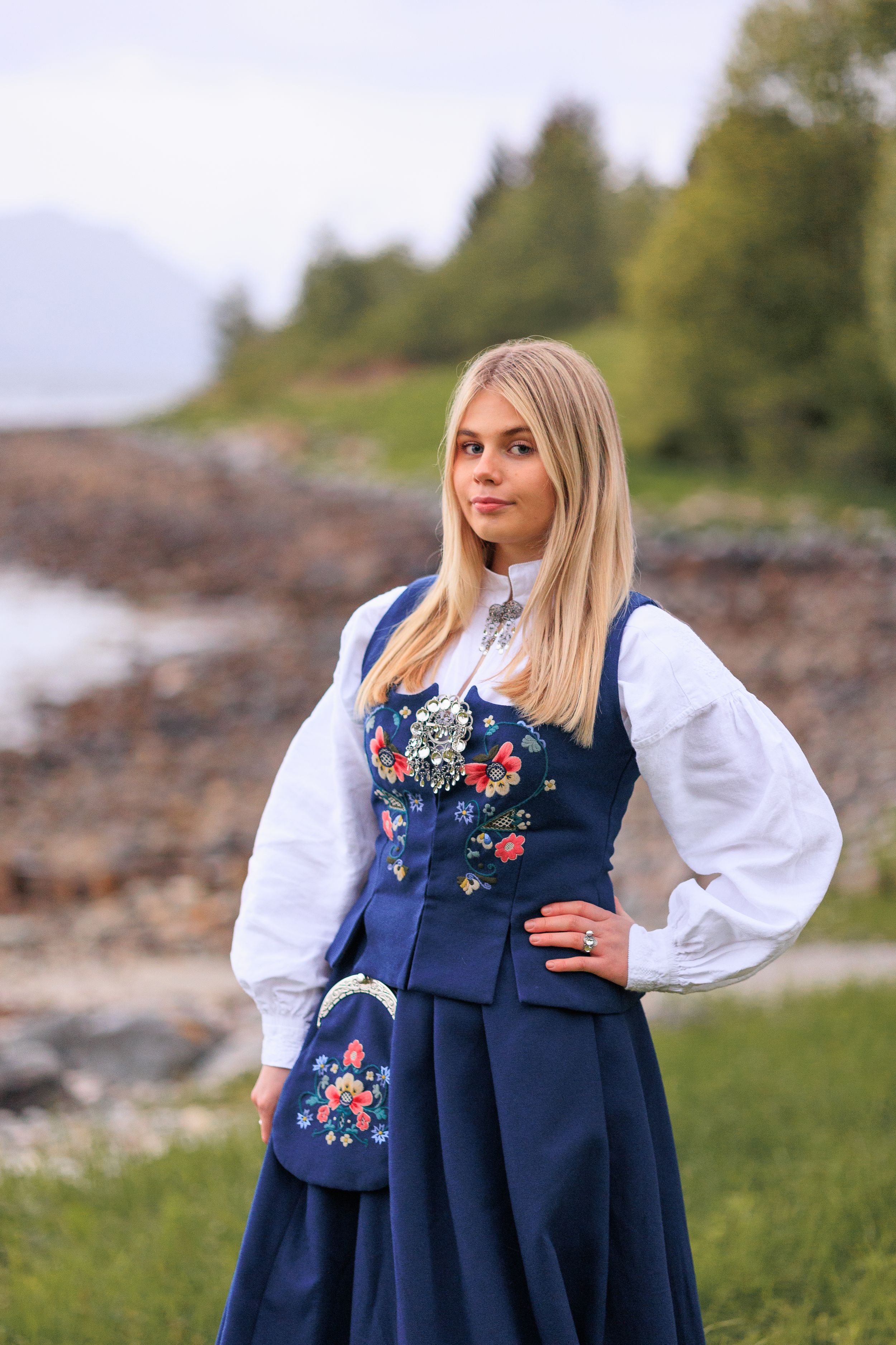 Traditional Norwegian bunad with embroidered details photographed against a coastal landscape.