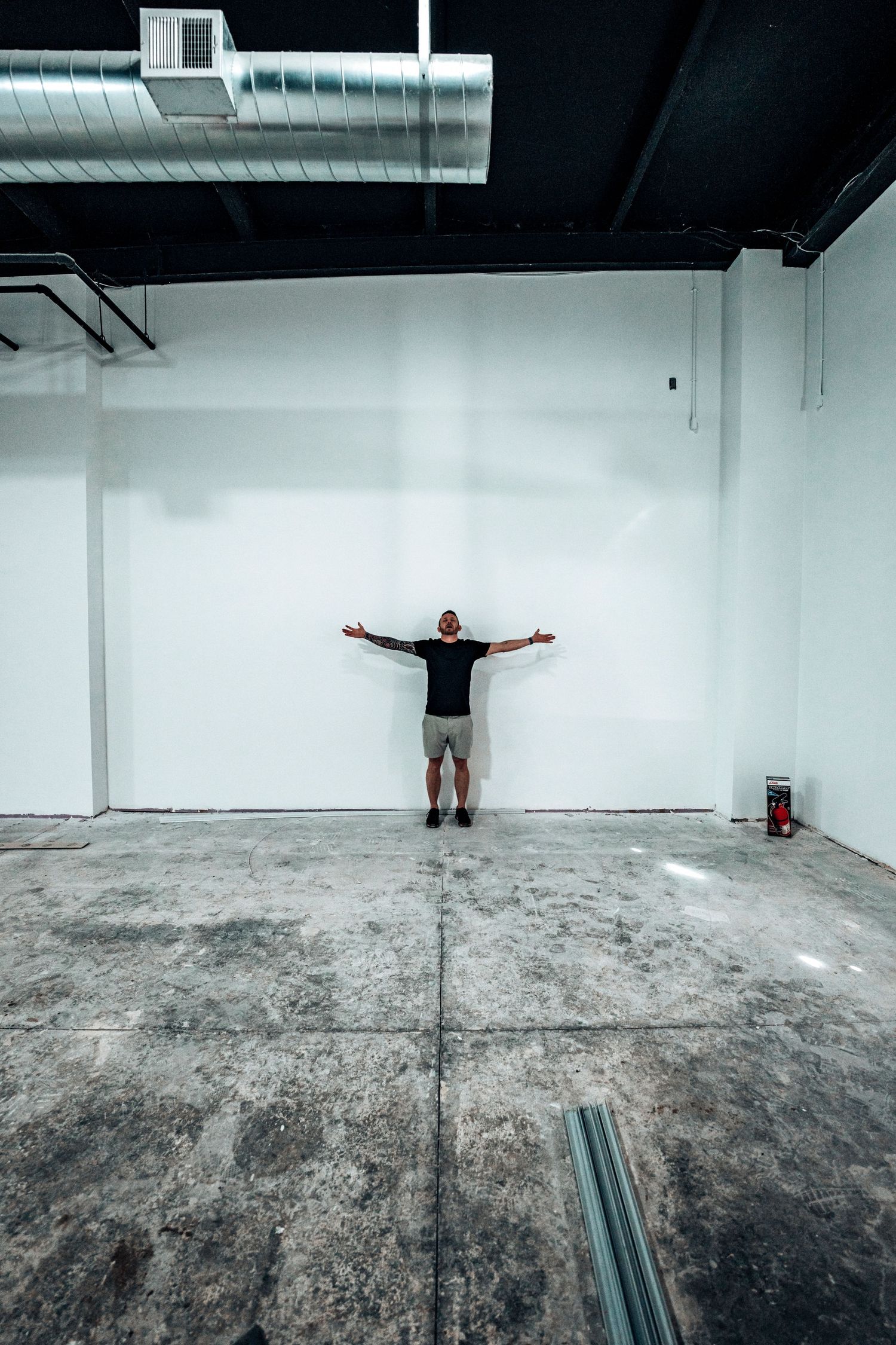 Person standing with arms spread wide against white wall in empty industrial space.