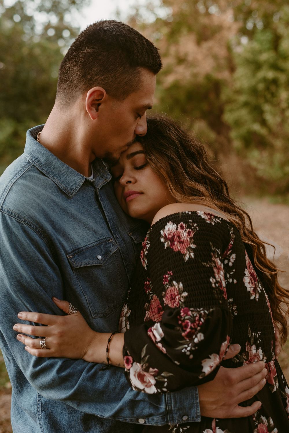 Tender embrace between couple in denim and floral dress during golden hour photo session.