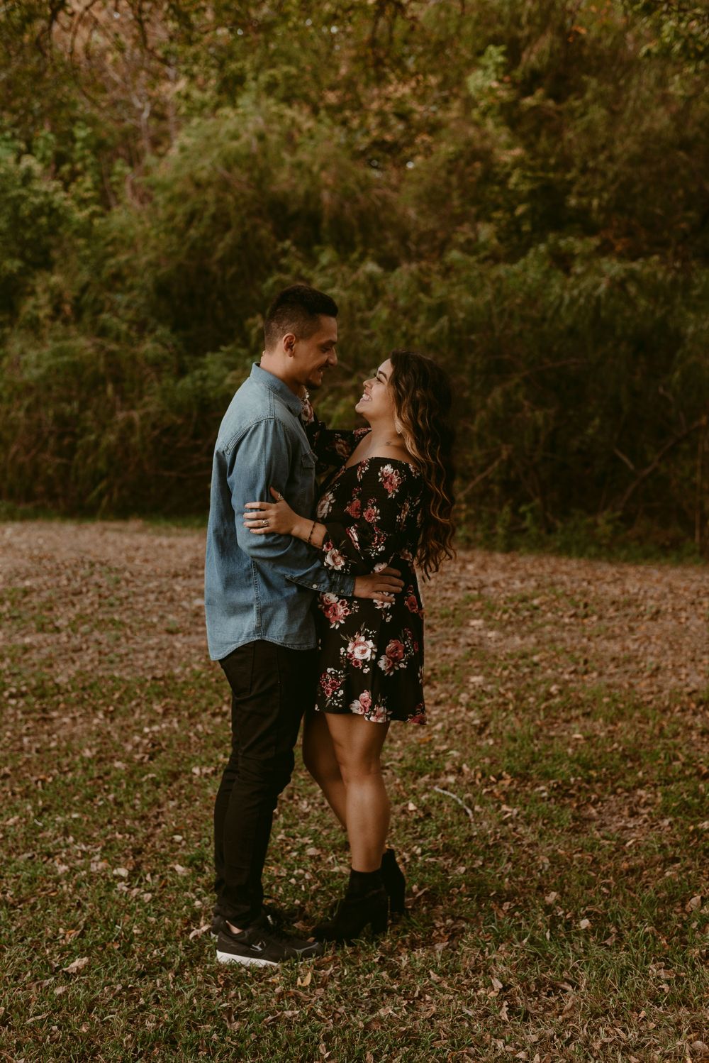 Couple shares tender moment while standing in autumn park with trees in background.