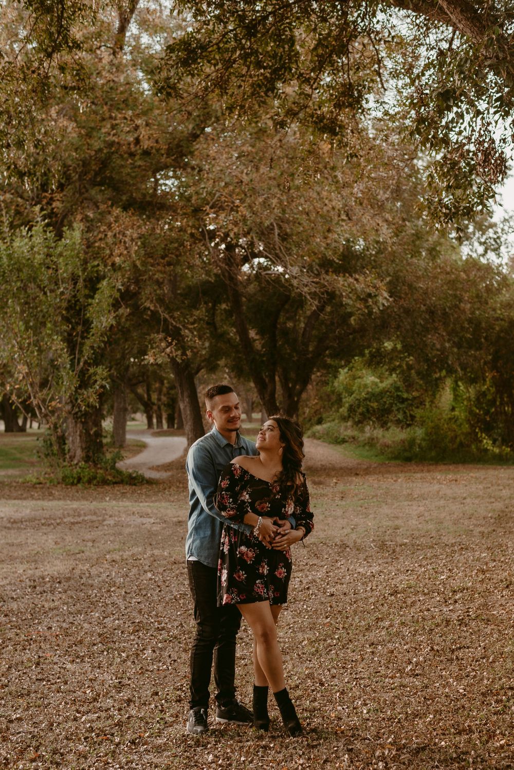 Couple embraces while standing in a peaceful wooded park during sunset.