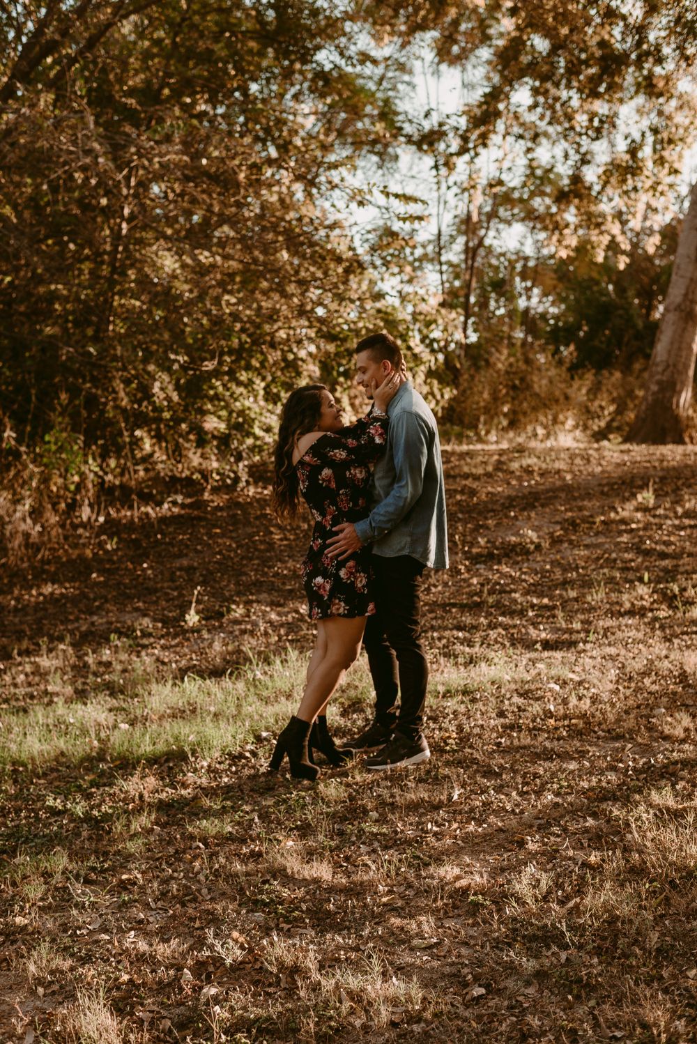 Romantic golden hour portrait of couple embracing in wooded park setting.