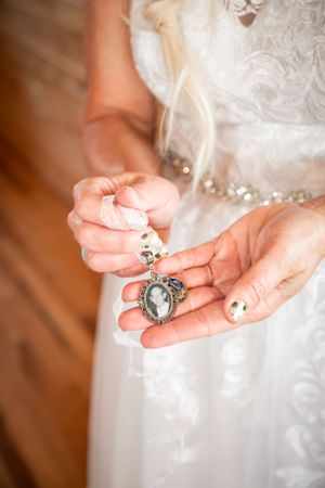Close up of hands holding an ornate vintage locket against a white lace dress.