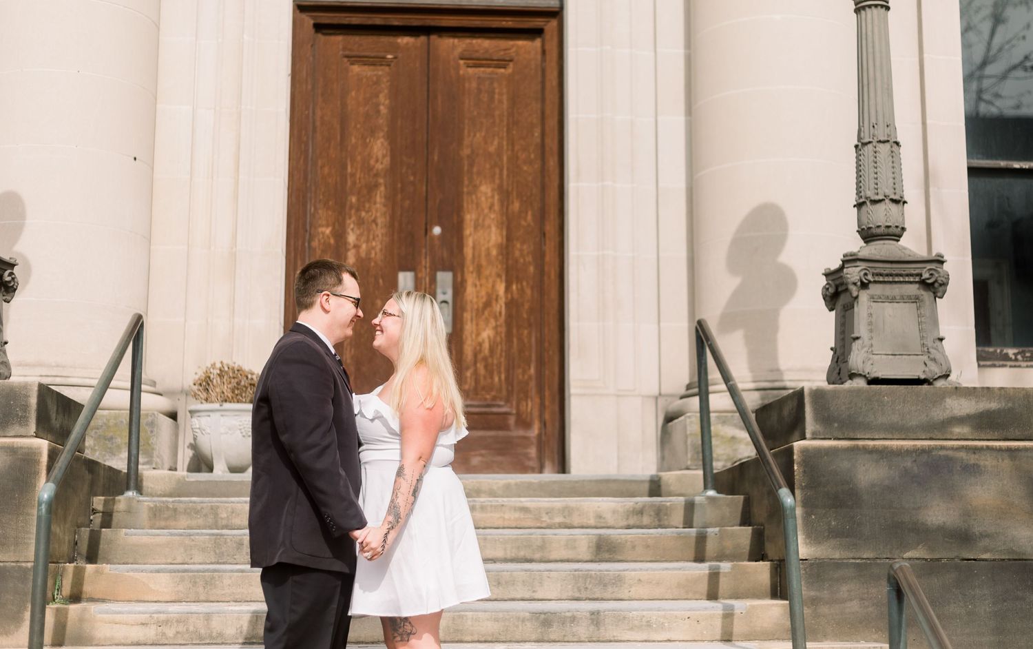 A couple embraces on stone steps with a vintage wooden door and iron railings in the background.