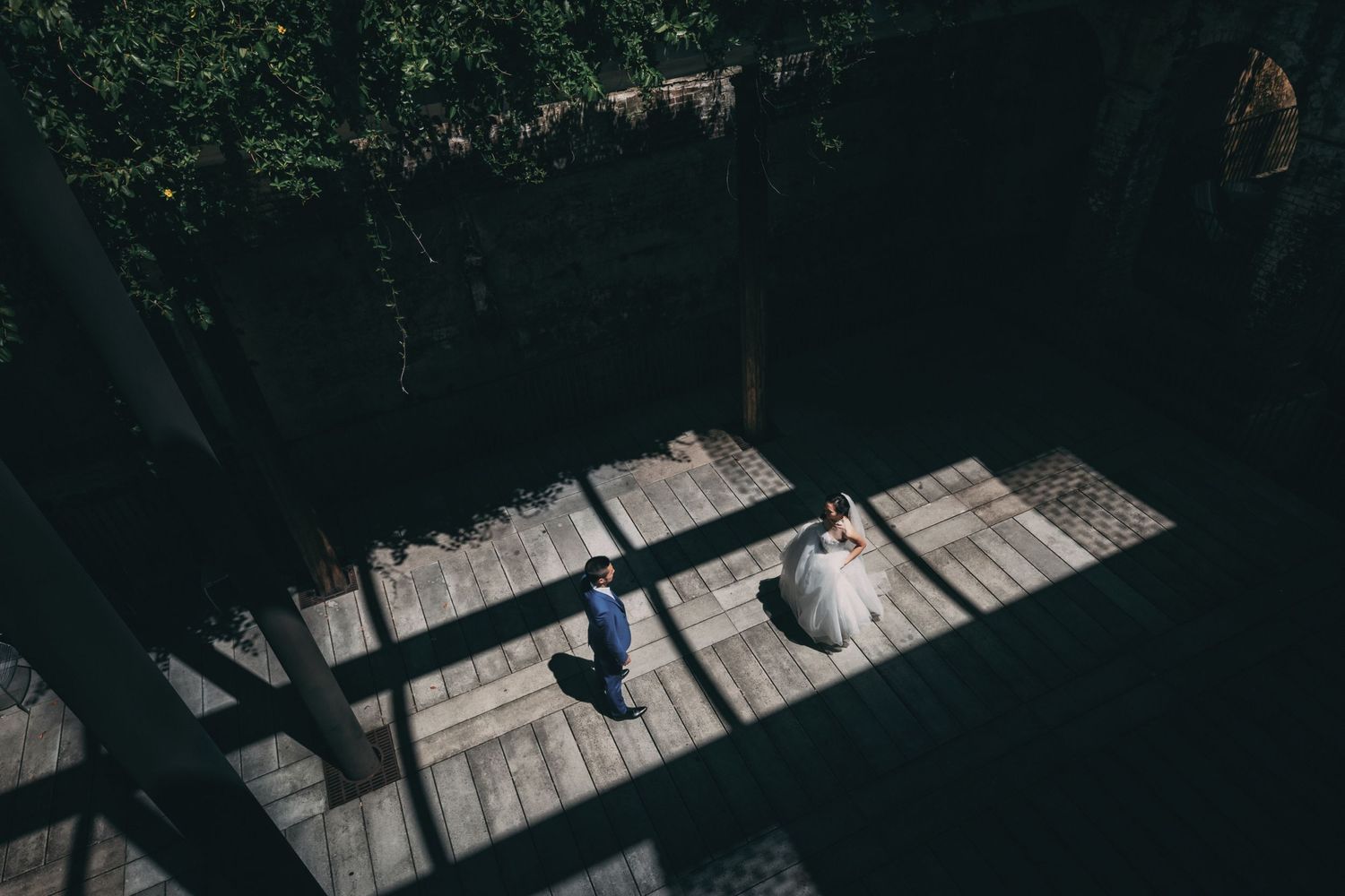 Aerial view of bride and groom on wooden deck with dramatic light and shadow patterns.