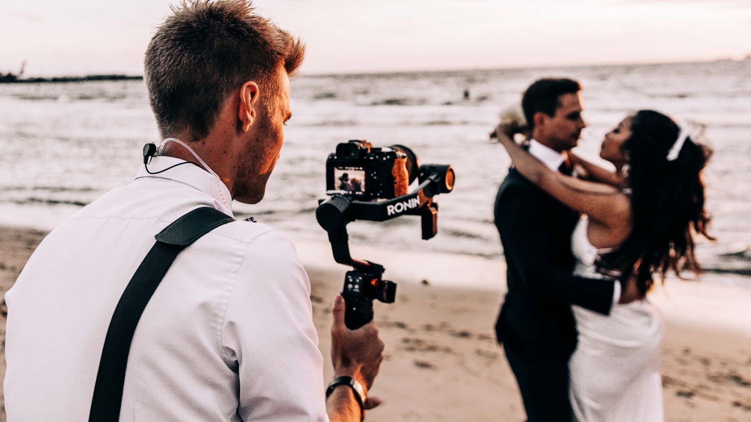 Wedding photographer capturing newlyweds dancing on a beach during sunset.