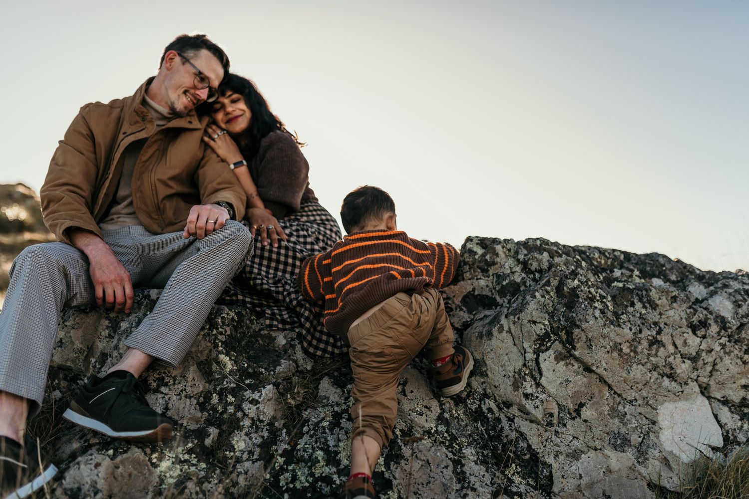 Family relaxing together on rocky terrain during sunset.