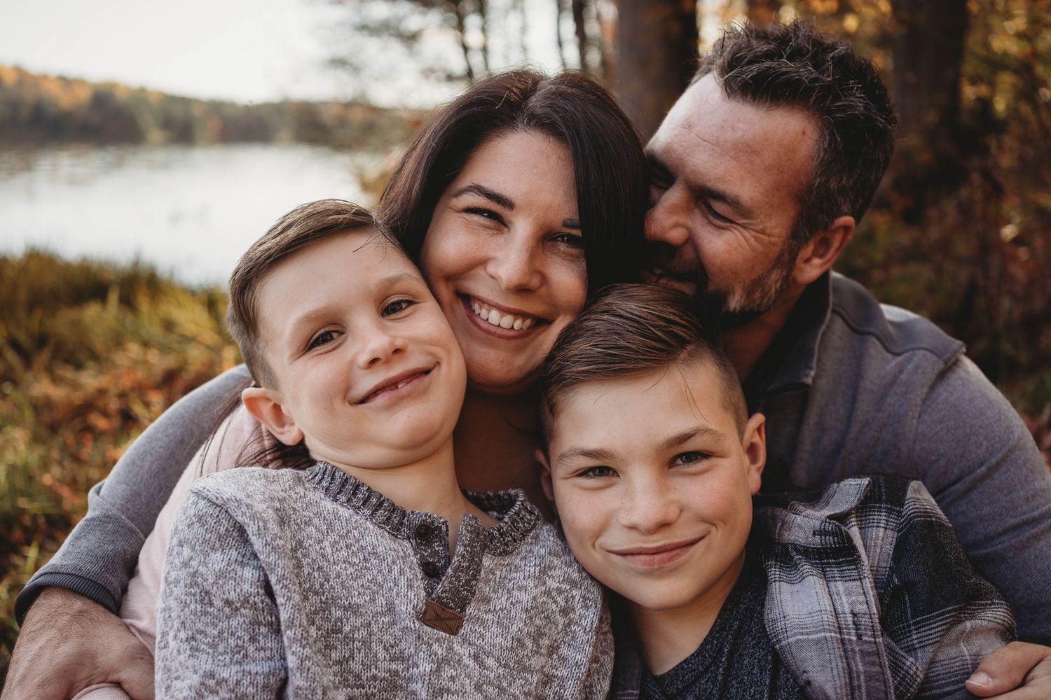 Close family portrait captured in autumn setting with lake and fall foliage in background.