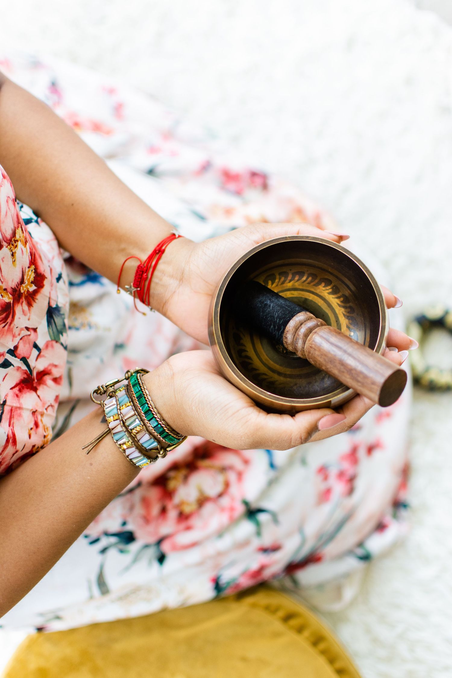 Hands holding traditional Tibetan singing bowl with turquoise bracelets and floral dress detail.