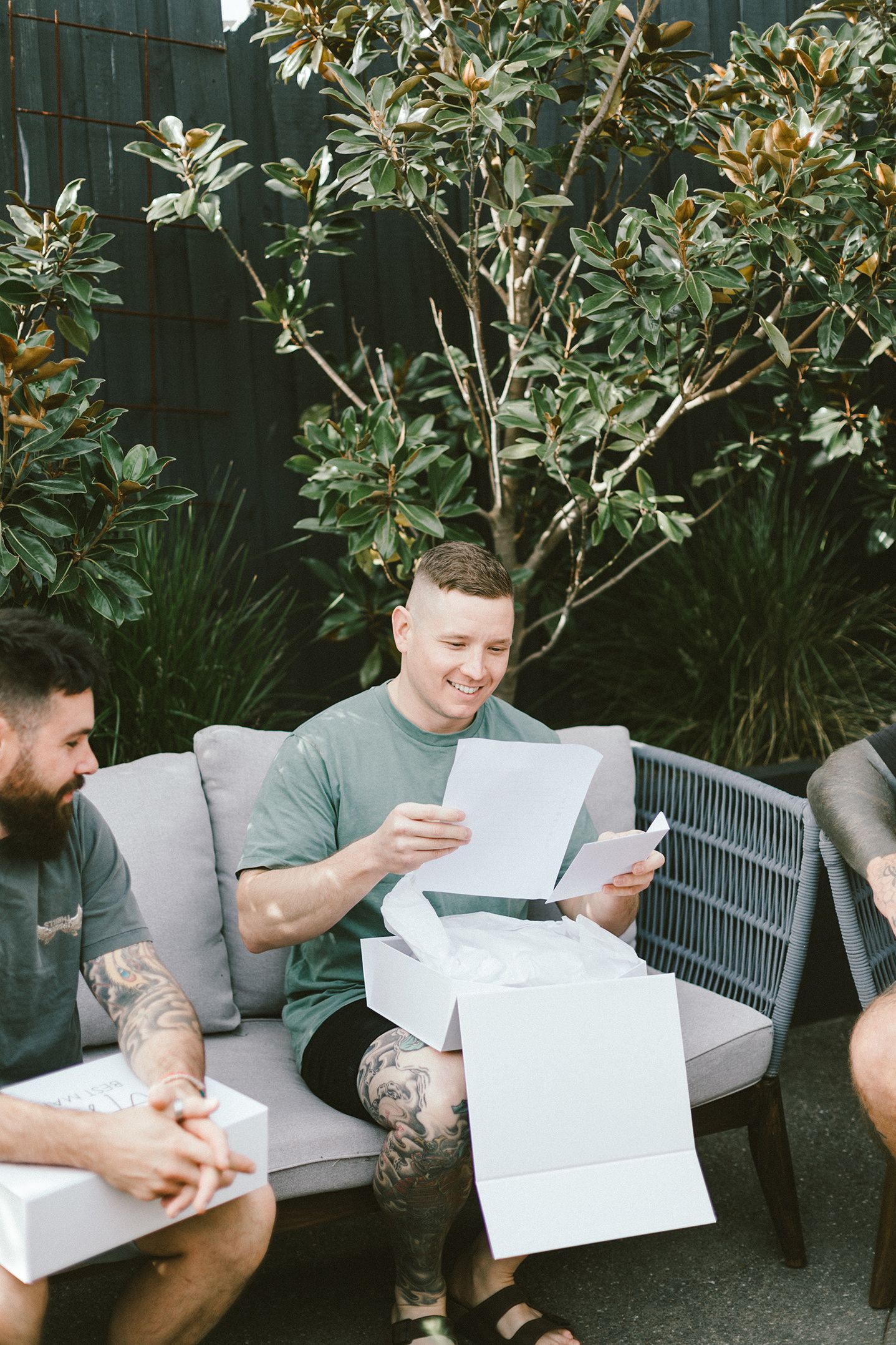 People reviewing documents while sitting on outdoor patio furniture with greenery backdrop.