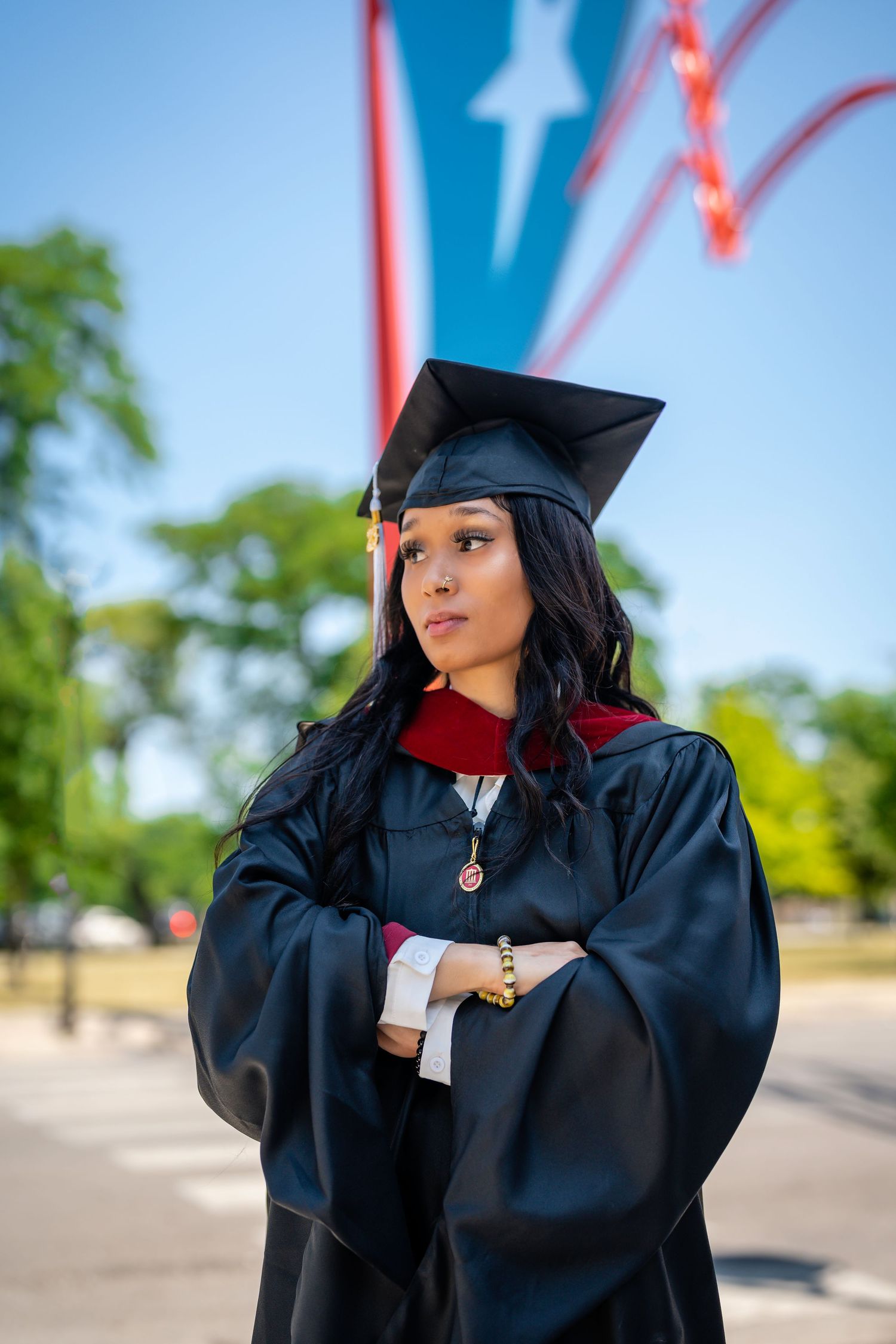 Graduate in black cap and gown poses outdoors against blue sky backdrop.