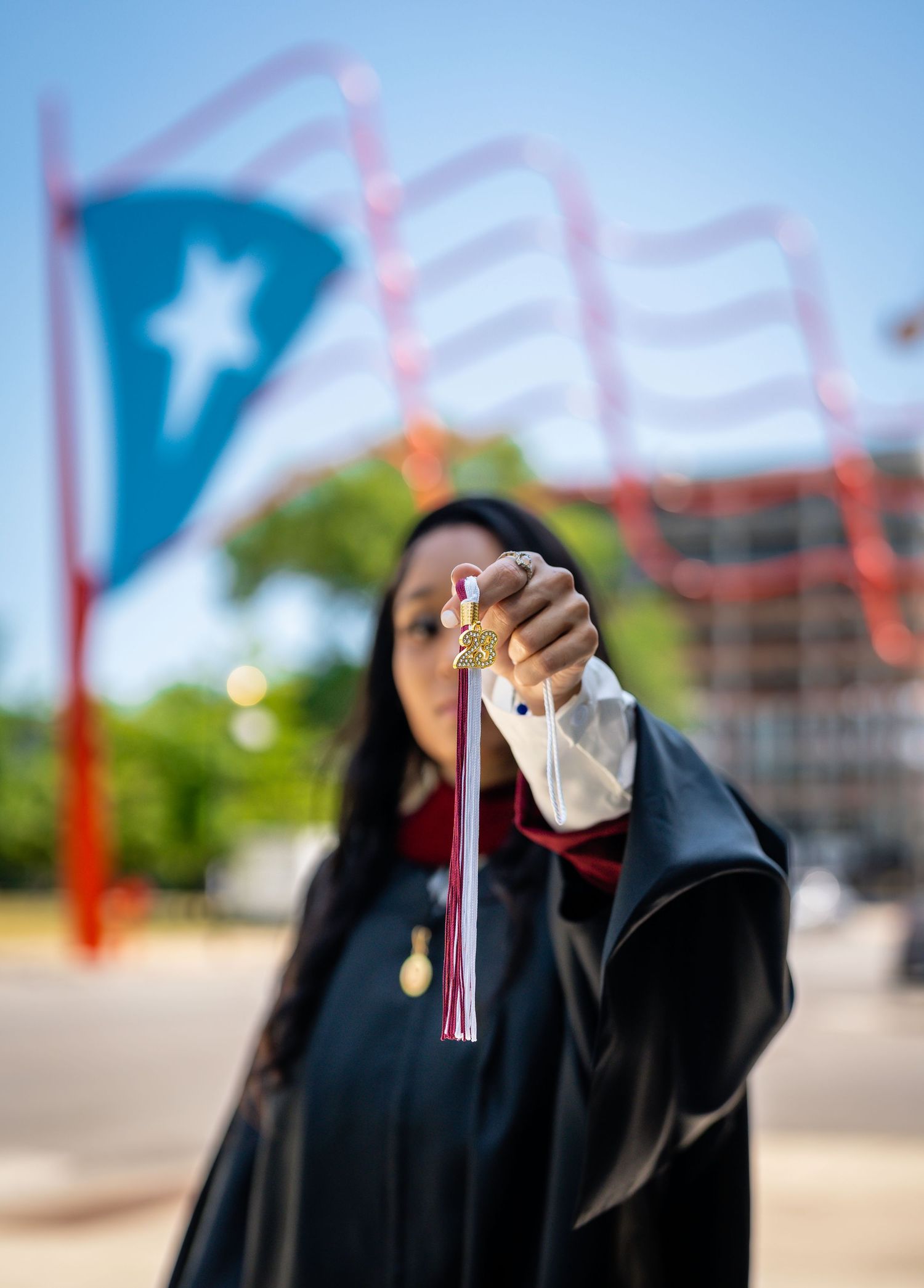 Graduate holds diploma up against bright blue sky in celebratory pose.