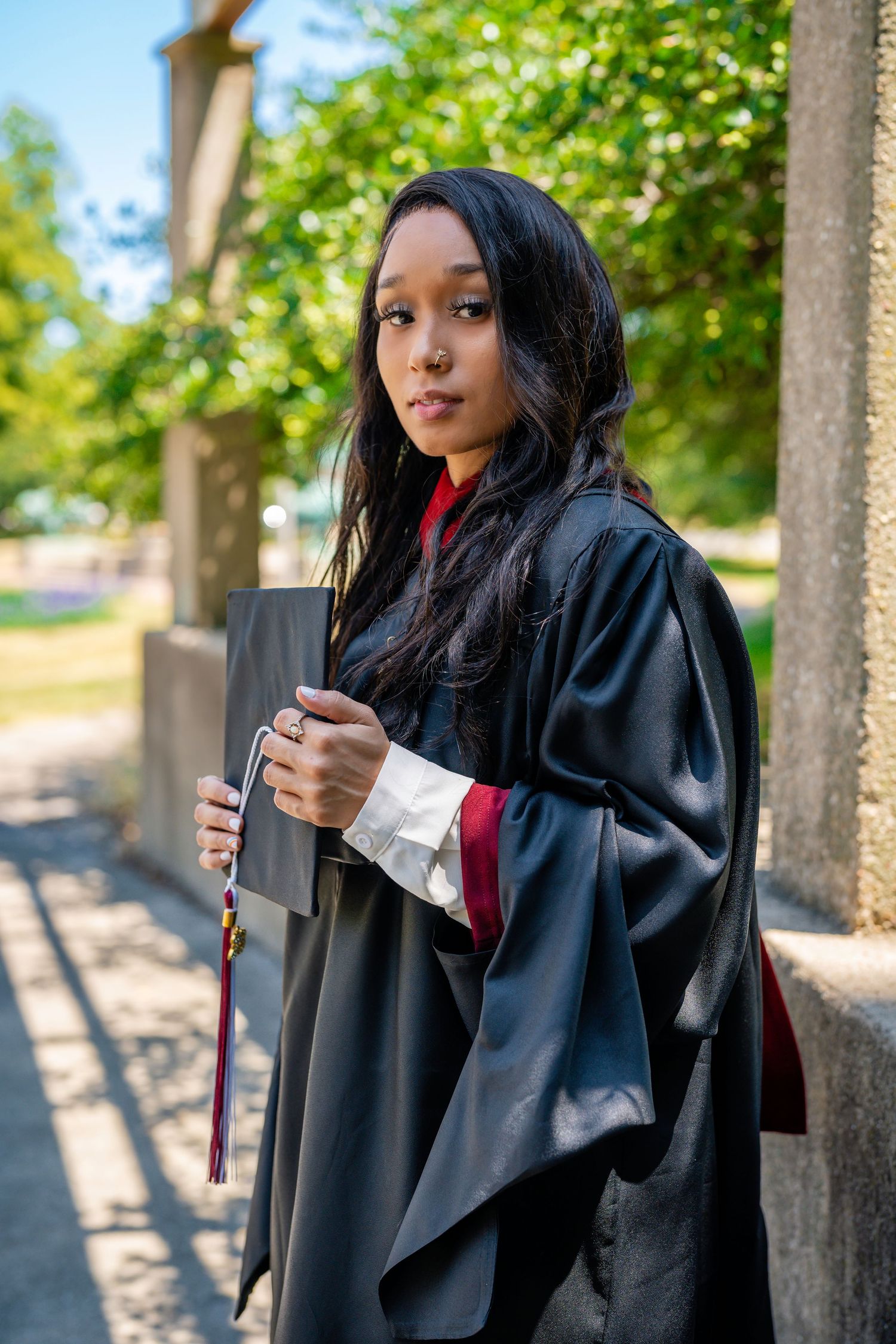 Graduate in black academic regalia poses in outdoor garden setting.