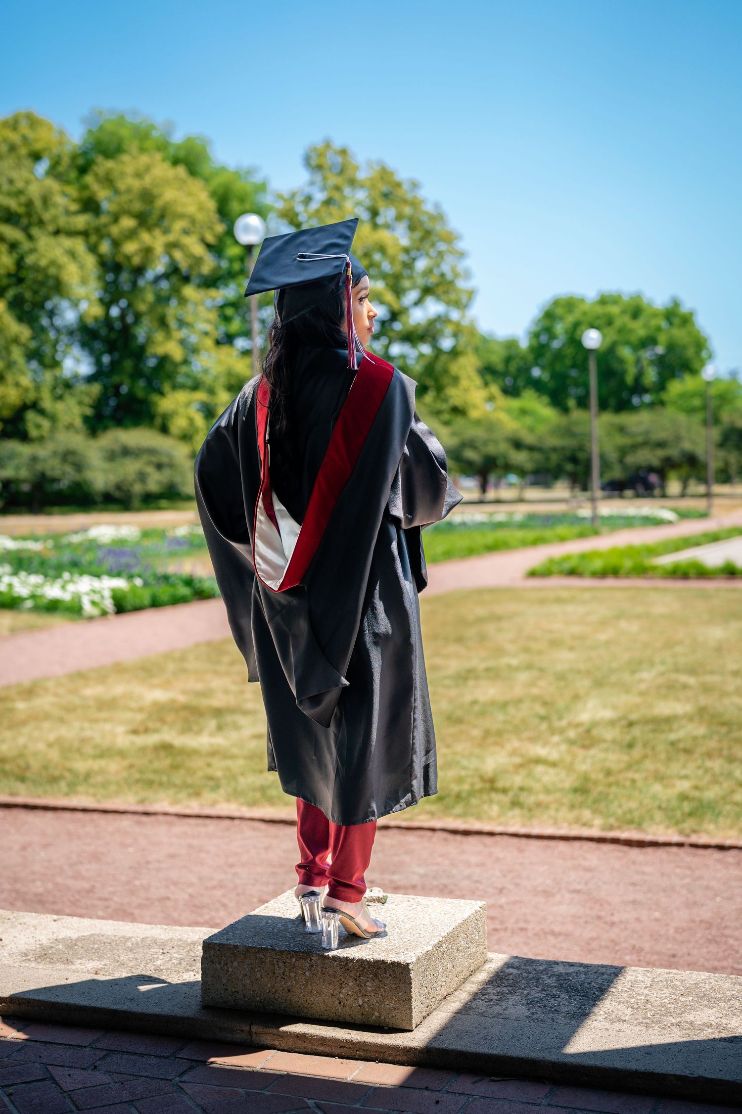 Graduate in academic regalia balances on concrete blocks in outdoor setting.