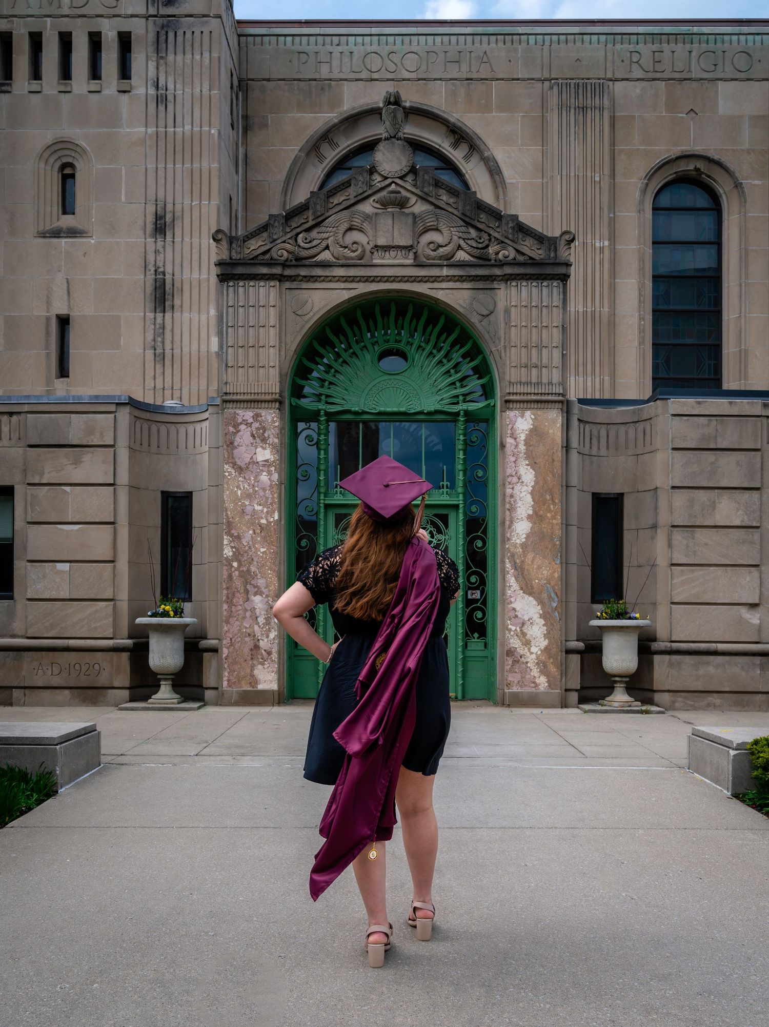 Graduate in burgundy stole poses in front of ornate stone building with green arched doorway.
