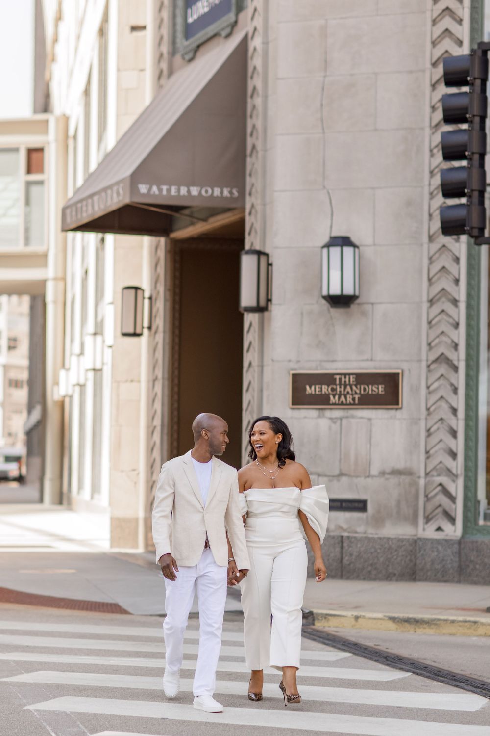 A couple in coordinated white outfits walks together near the Waterworks building entrance.
