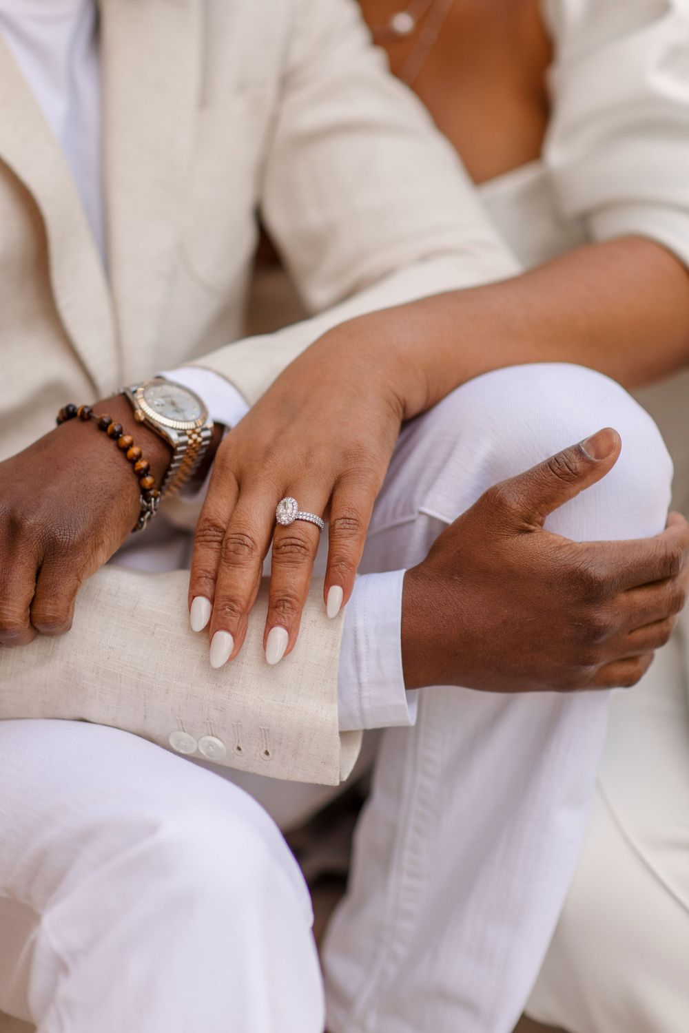 Close-up detail shot of hands wearing white clothing, jewelry and a watch.