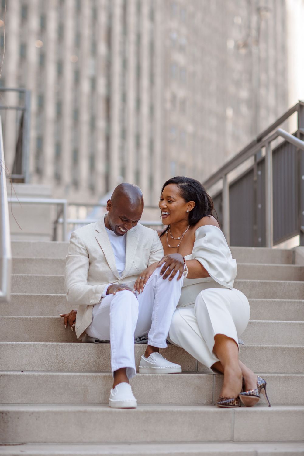 A candid moment of a couple in coordinating white outfits sitting on urban steps.