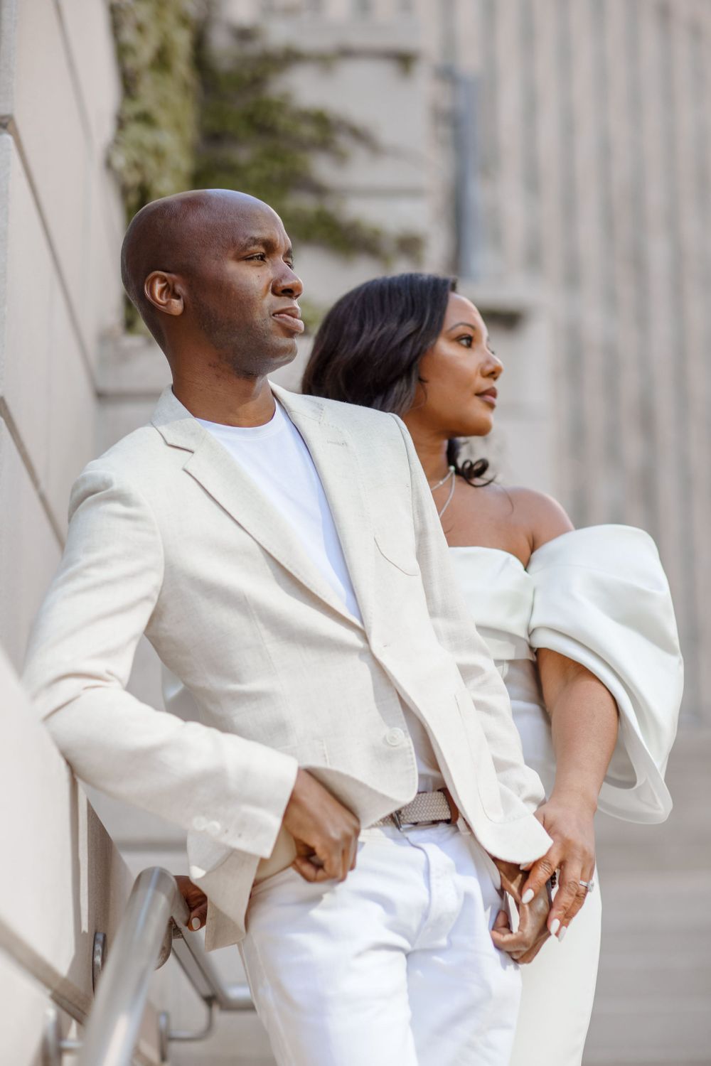 Sophisticated couple in white ensembles posing against an urban backdrop.