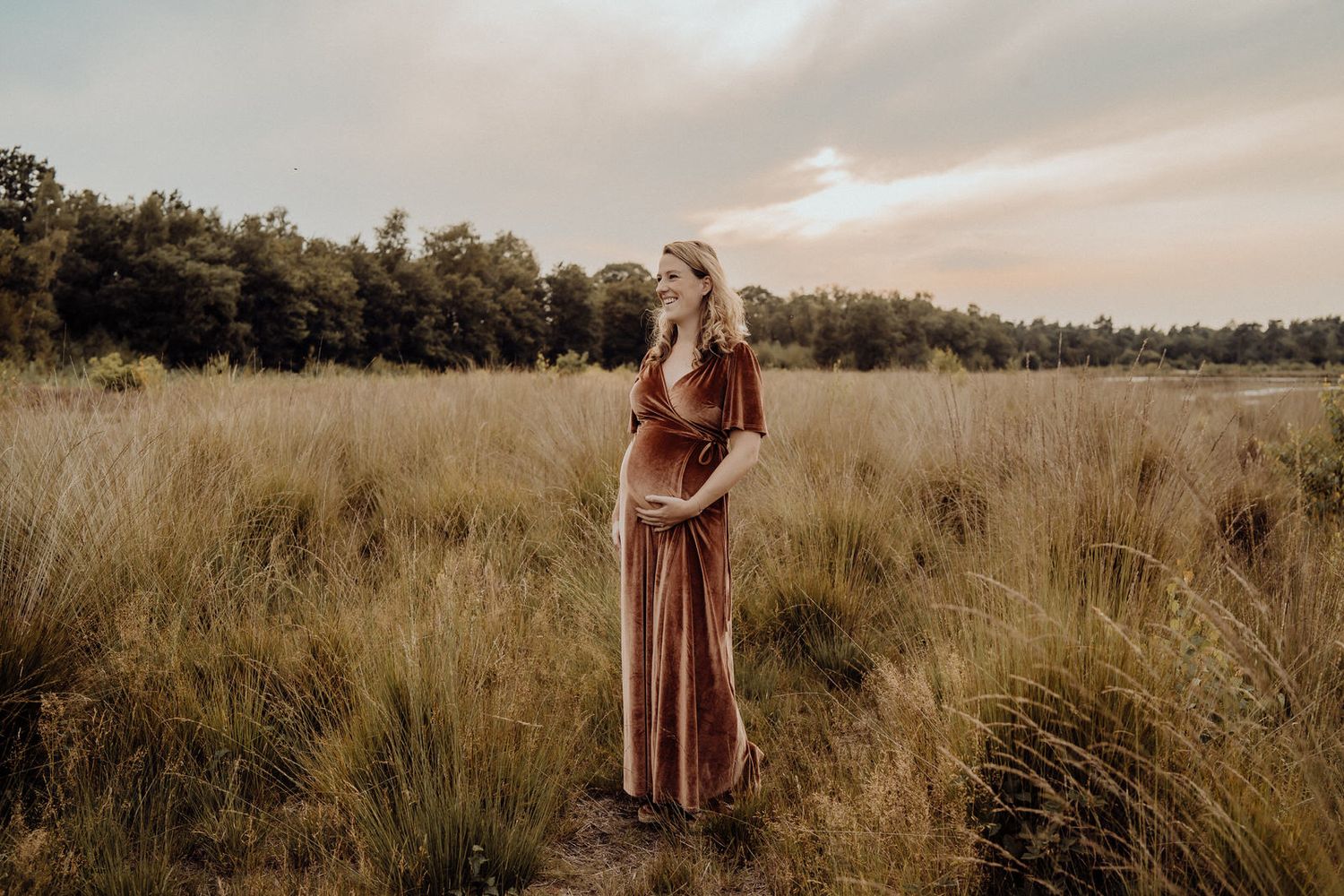Ethereal pregnancy portrait in a rustic field during sunset with a flowing burgundy dress.
