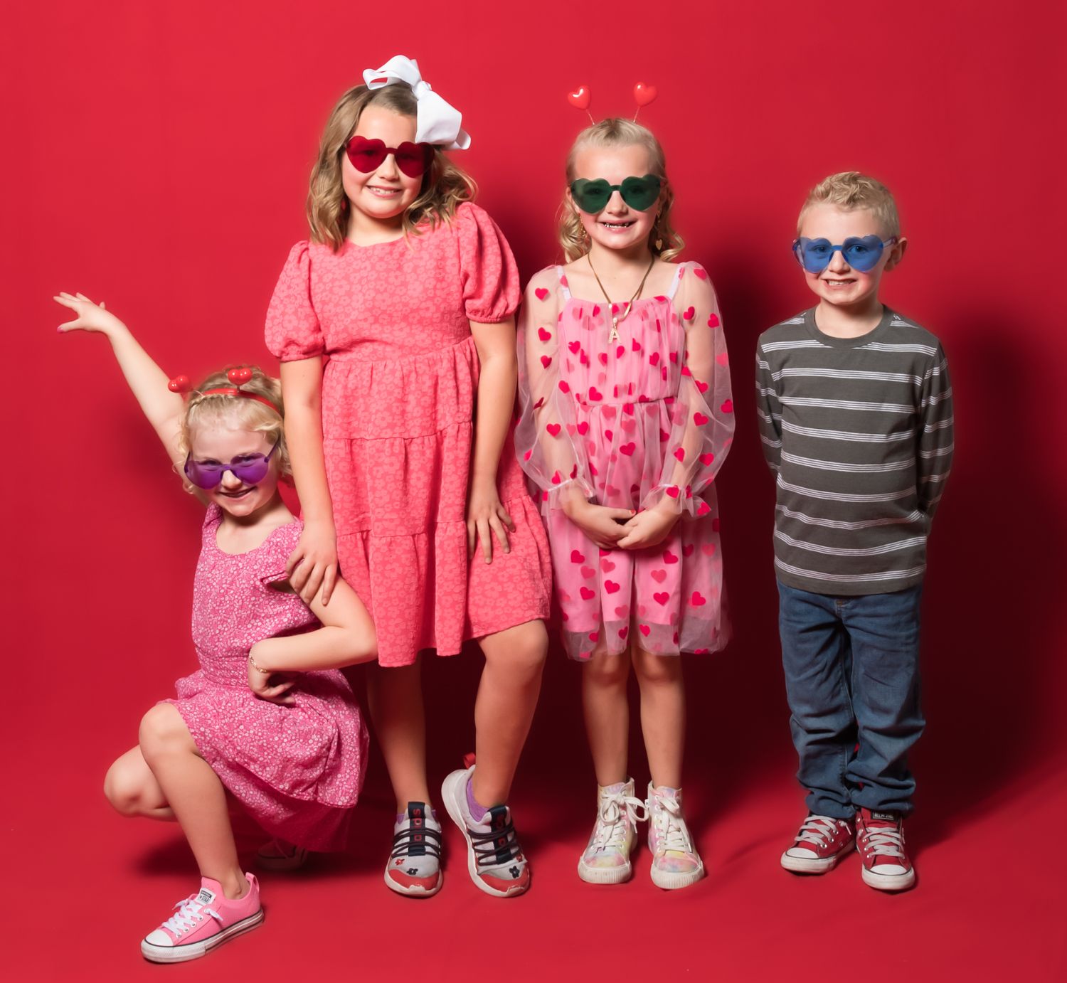 Group of children wearing coordinated pink and red outfits posing against red backdrop.