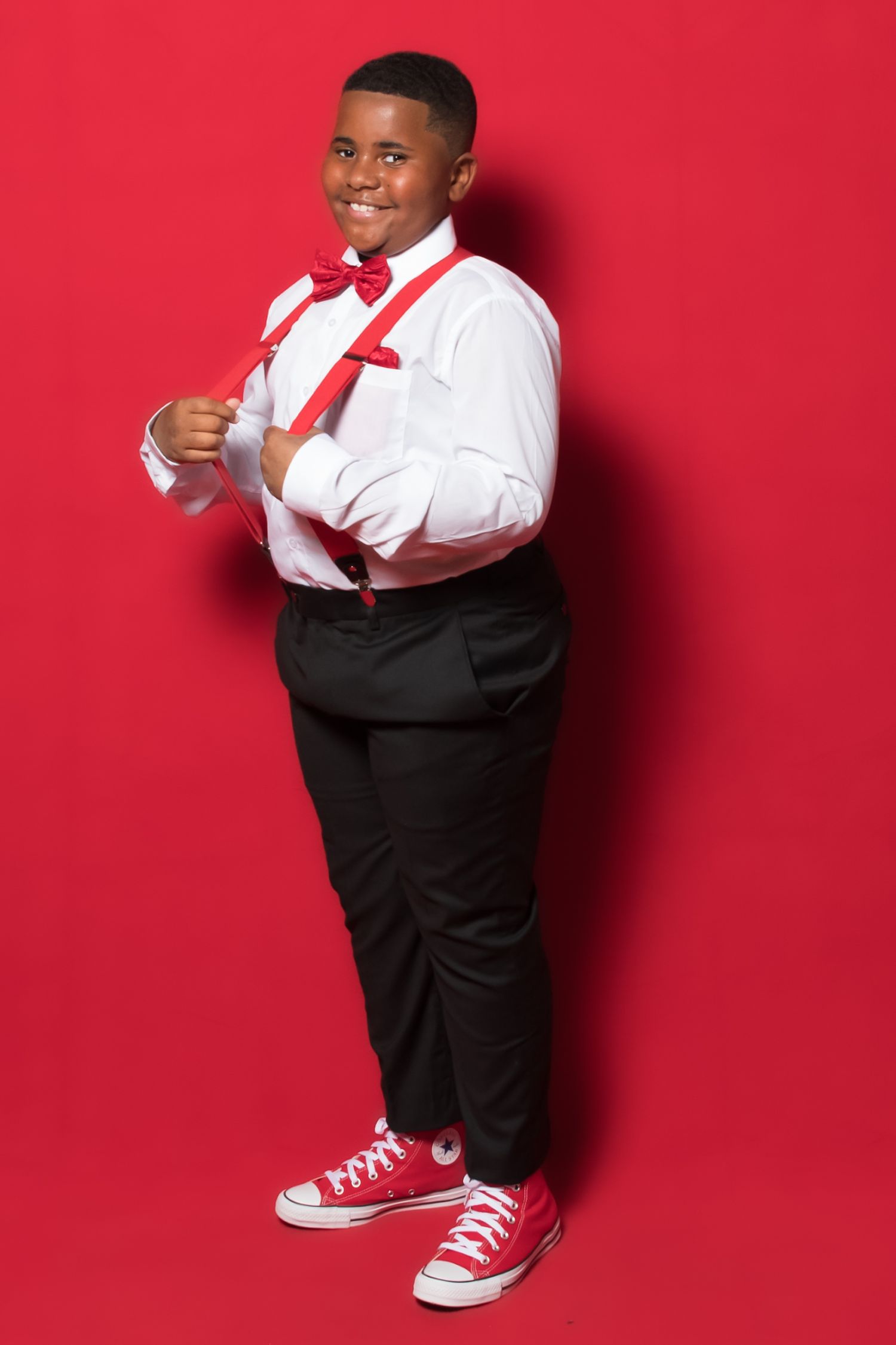 Festive outfit combination with suspenders and bow tie styled against vibrant red backdrop.
