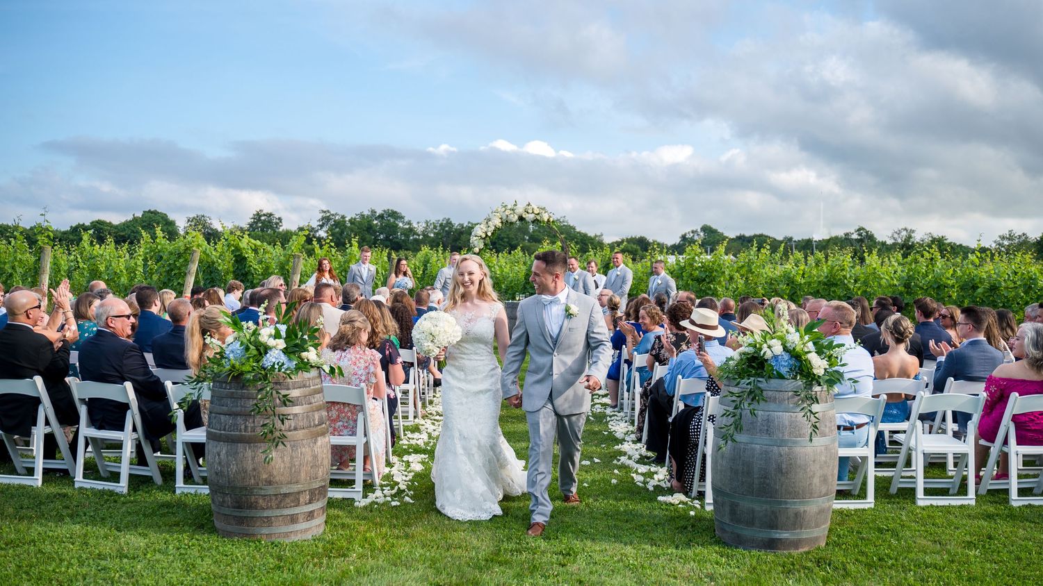 Couple happily walking hand in hand away from their ceremony in the vineyards.